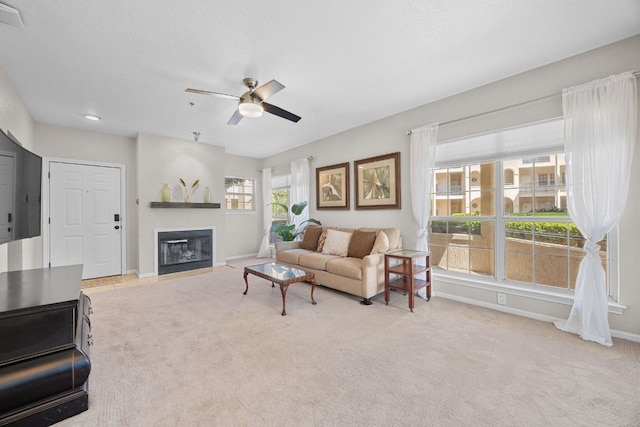 carpeted living room with a fireplace with flush hearth, baseboards, and ceiling fan