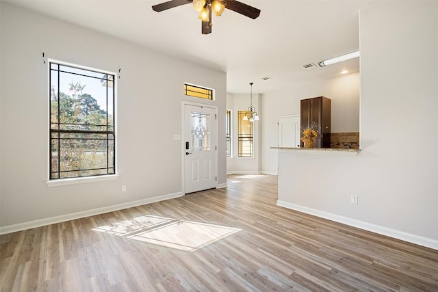 unfurnished living room featuring ceiling fan, plenty of natural light, light wood-style floors, and baseboards