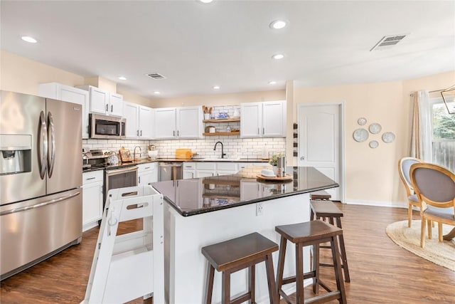 kitchen with appliances with stainless steel finishes, a kitchen bar, a sink, open shelves, and backsplash