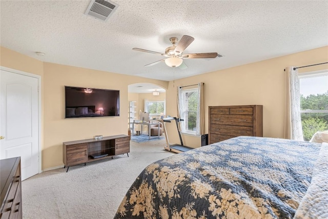 carpeted bedroom featuring multiple windows, arched walkways, a textured ceiling, a ceiling fan, and baseboards
