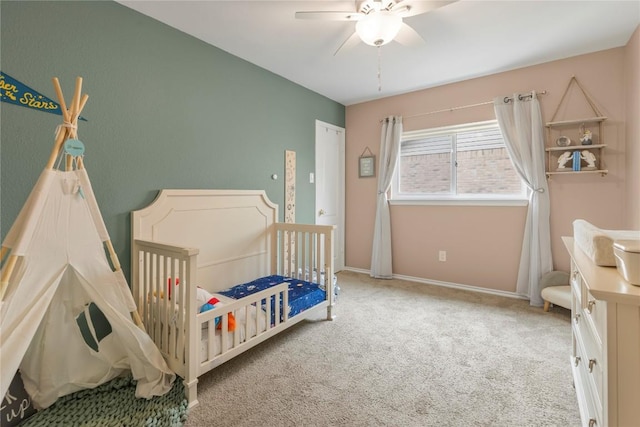 bedroom with carpet flooring, baseboards, a crib, and a ceiling fan