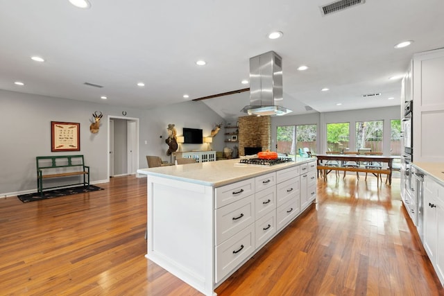5911 W Gate Blvd, Austin, TX 78745 - kitchen featuring island range hood, stainless steel gas stovetop, wood finished floors, a center island, and light countertops