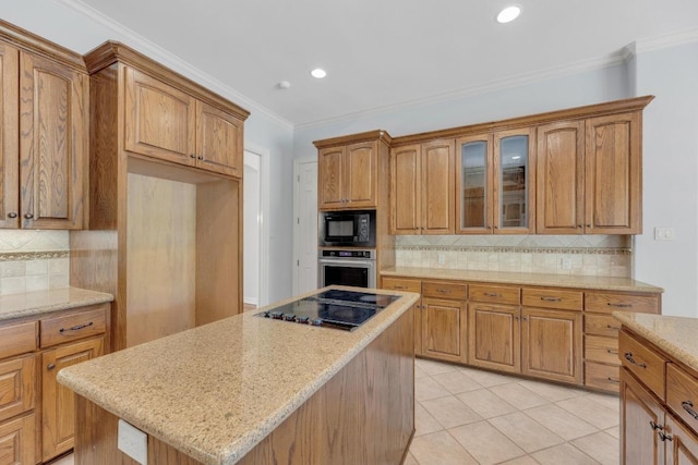 kitchen with a center island, brown cabinetry, black appliances, light stone countertops, and backsplash