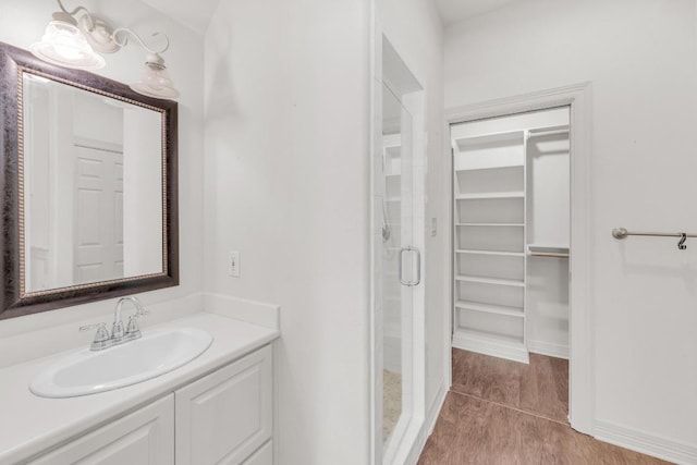 bathroom with a spacious closet, a shower stall, vanity, and baseboards