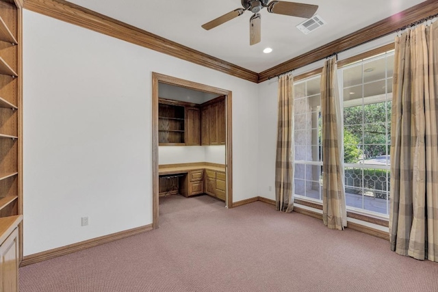 spare room with baseboards, built in desk, light carpet, crown molding, and visible vents