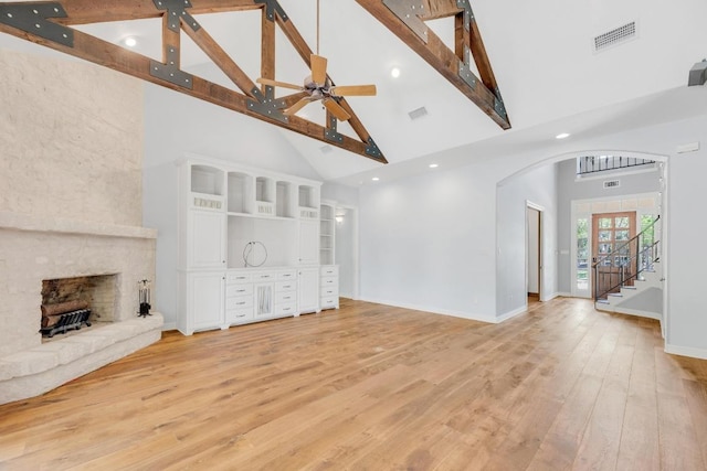 unfurnished living room with visible vents, arched walkways, light wood-style floors, a large fireplace, and high vaulted ceiling