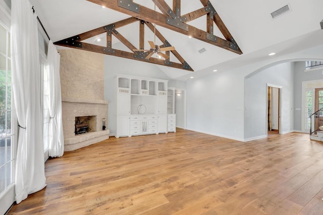unfurnished living room with baseboards, arched walkways, a fireplace, beamed ceiling, and high vaulted ceiling