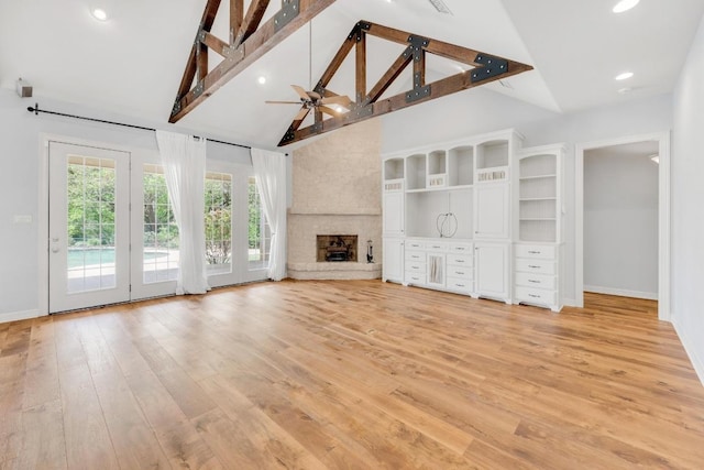 unfurnished living room with high vaulted ceiling, a fireplace, a ceiling fan, light wood finished floors, and baseboards