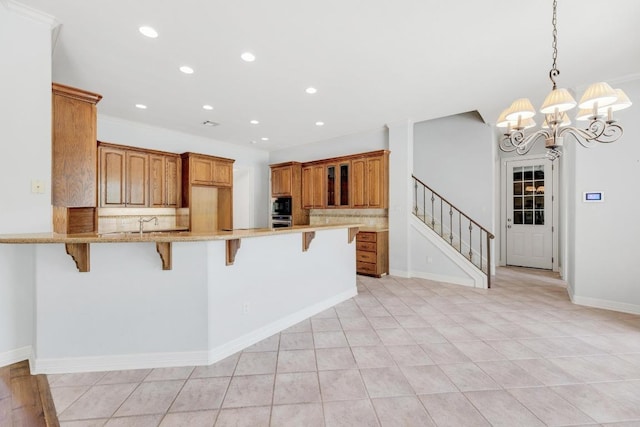 kitchen with a peninsula, a notable chandelier, a kitchen bar, and stainless steel oven
