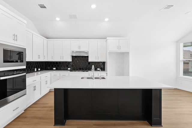 220 Washington Dr, Kyle, TX 78640 - kitchen with a sink, vaulted ceiling, under cabinet range hood, cooktop, and decorative backsplash
