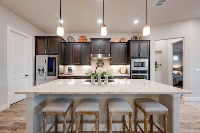 262 Singing Sumac Way, San Marcos, TX 78666 - kitchen with stainless steel appliances, a kitchen breakfast bar, a kitchen island with sink, tasteful backsplash, and dark brown cabinets