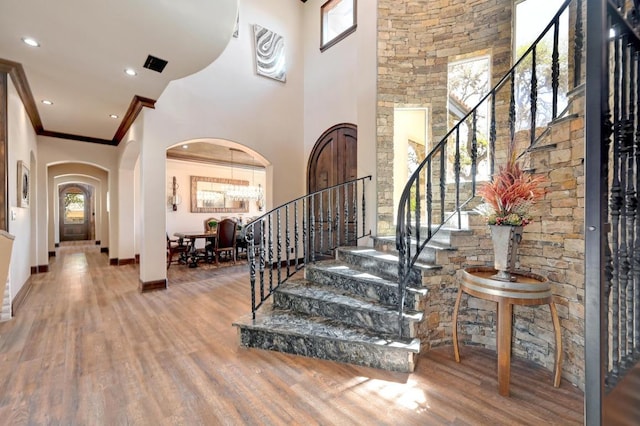 foyer entrance with arched walkways, stairway, crown molding, and wood finished floors