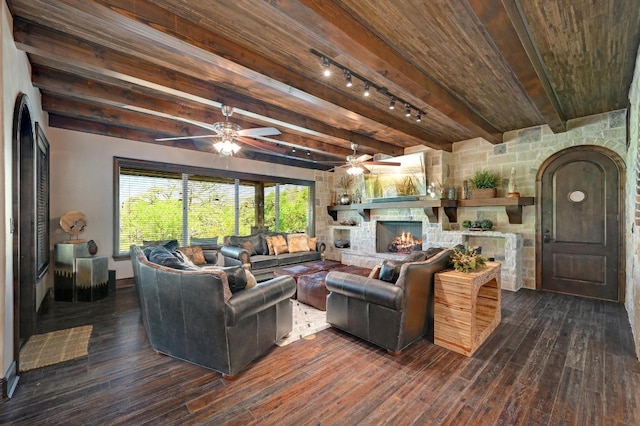 living room featuring ceiling fan, dark wood-type flooring, track lighting, a stone fireplace, and wood ceiling