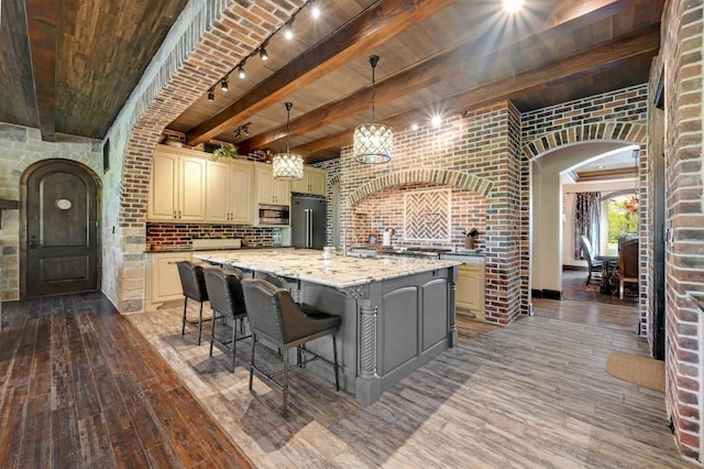 kitchen featuring brick wall, cream cabinetry, hardwood / wood-style floors, appliances with stainless steel finishes, and arched walkways