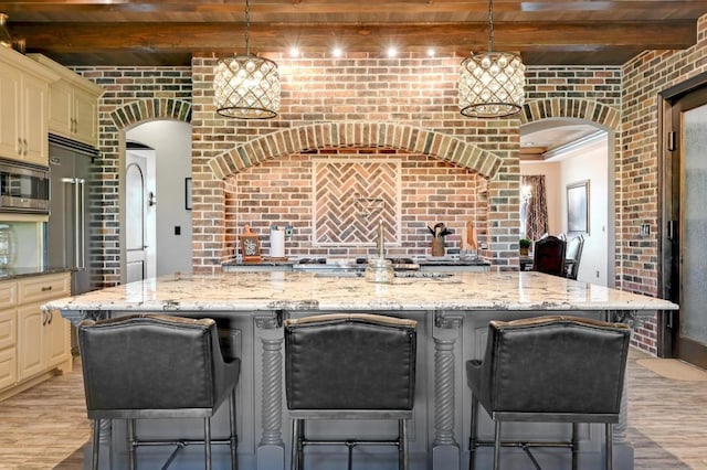 kitchen featuring brick wall, light wood-type flooring, appliances with stainless steel finishes, beamed ceiling, and cream cabinets