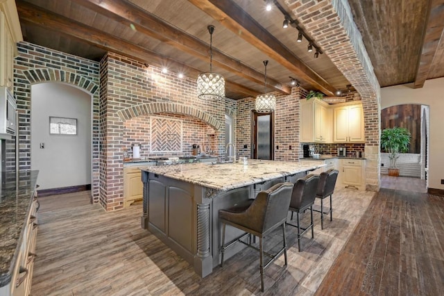 kitchen featuring wood finished floors, a kitchen island with sink, cream cabinets, baseboards, and beam ceiling