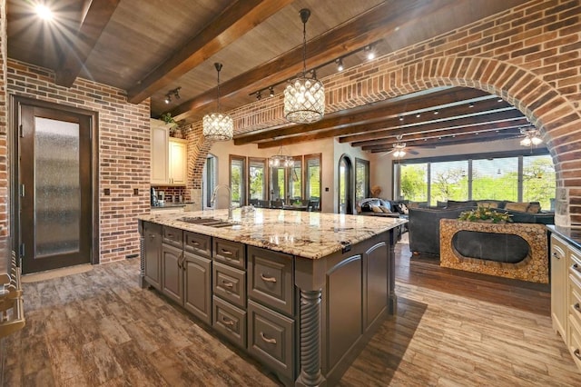 kitchen featuring brick wall, an island with sink, dark wood-style flooring, and a sink