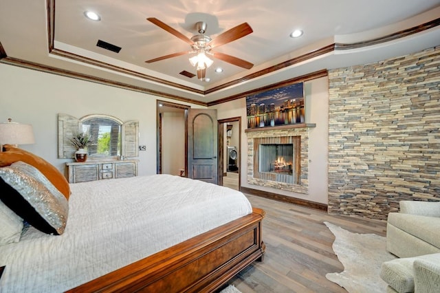 bedroom featuring a fireplace, a tray ceiling, ornamental molding, recessed lighting, and wood finished floors