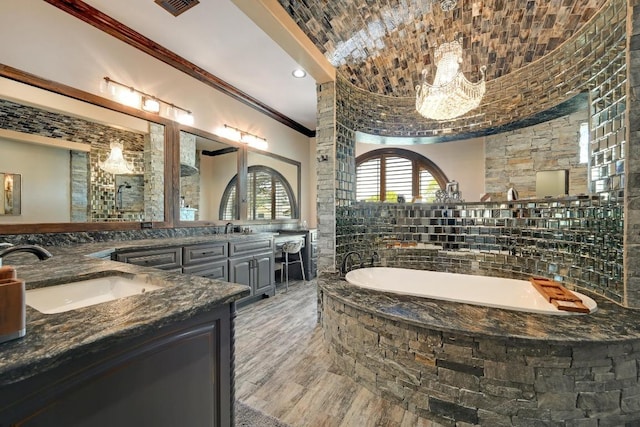 bathroom with double vanity, ornamental molding, a bath, a sink, and wood finished floors