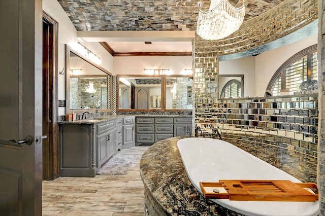 bathroom with a notable chandelier, ornamental molding, a freestanding bath, a sink, and wood finished floors