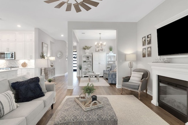 121 Monterey Oak Trl, Georgetown, TX 78628 - living room with baseboards, a glass covered fireplace, recessed lighting, wood finished floors, and ceiling fan with notable chandelier