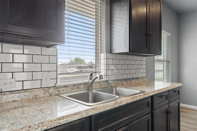 kitchen with dark brown cabinetry, baseboards, backsplash, light wood finished floors, and a sink