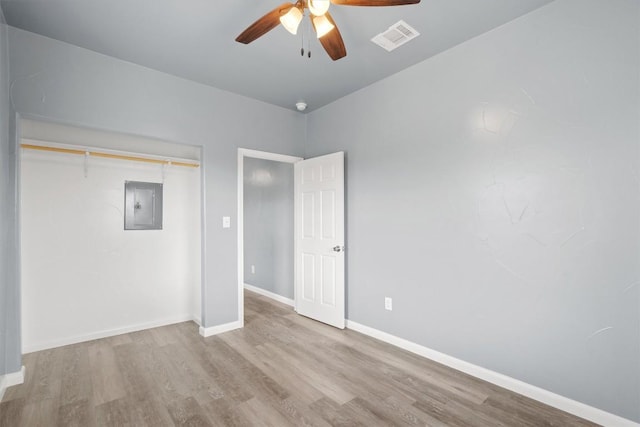 unfurnished bedroom featuring baseboards, a closet, electric panel, visible vents, and wood finished floors