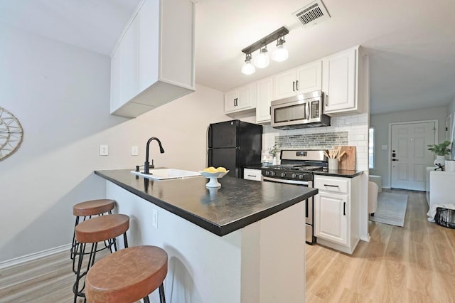 3309 Clawson Rd, Austin, TX 78704 - kitchen featuring appliances with stainless steel finishes, dark countertops, a sink, light wood-style floors, and a breakfast bar