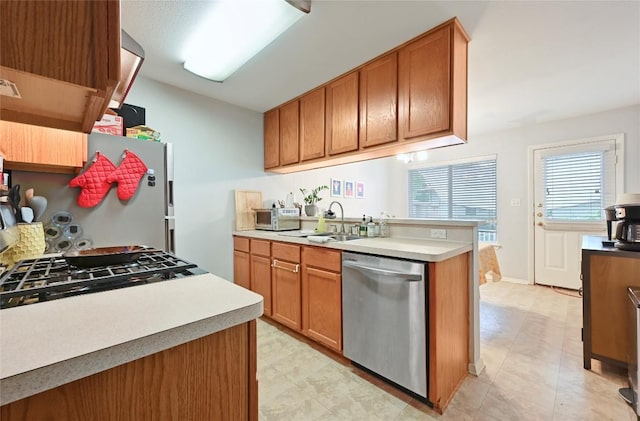 kitchen with brown cabinetry, stainless steel dishwasher, freestanding refrigerator, and a sink