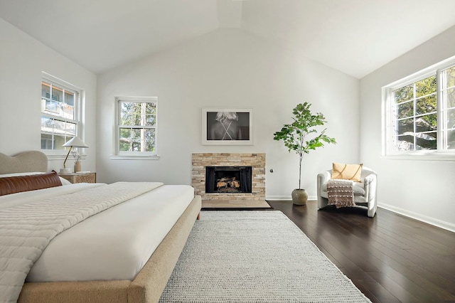bedroom featuring a fireplace with flush hearth, vaulted ceiling, dark wood-style floors, and multiple windows