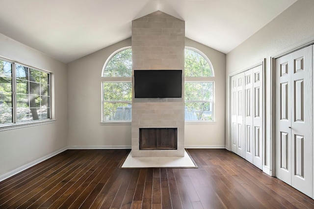 unfurnished living room with vaulted ceiling, a tiled fireplace, wood finished floors, and plenty of natural light