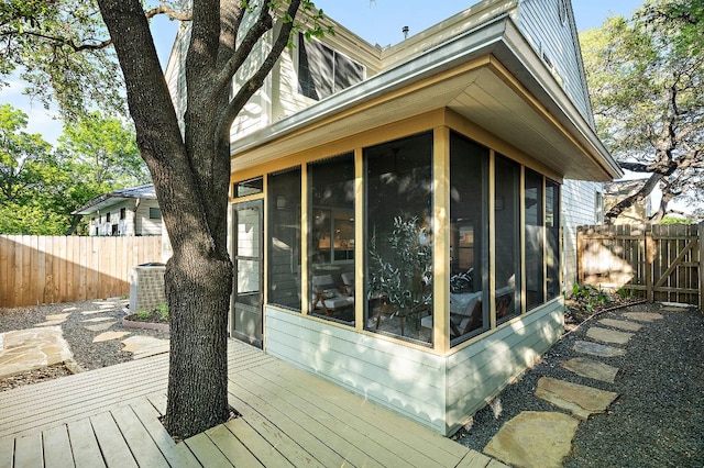 view of side of property with a fenced backyard, a wooden deck, a sunroom, and central air condition unit
