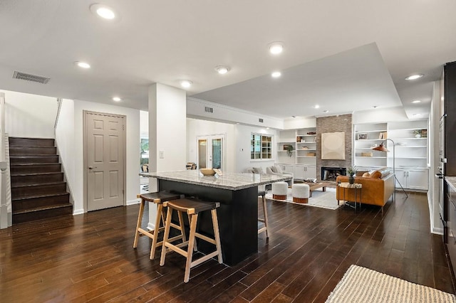 kitchen with a kitchen bar, light stone countertops, visible vents, and dark wood-style floors