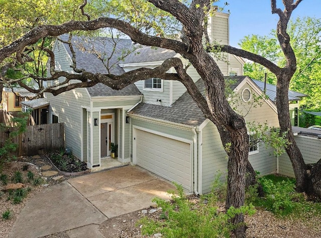 view of front of property featuring a chimney, concrete driveway, fence, a garage, and a shingled roof