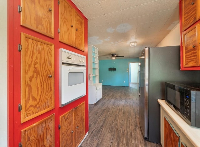 kitchen with ceiling fan, white oven, black microwave, brown cabinetry, and dark wood-style floors