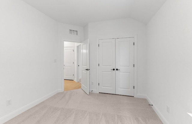 unfurnished bedroom with light carpet, vaulted ceiling, baseboards, and a closet