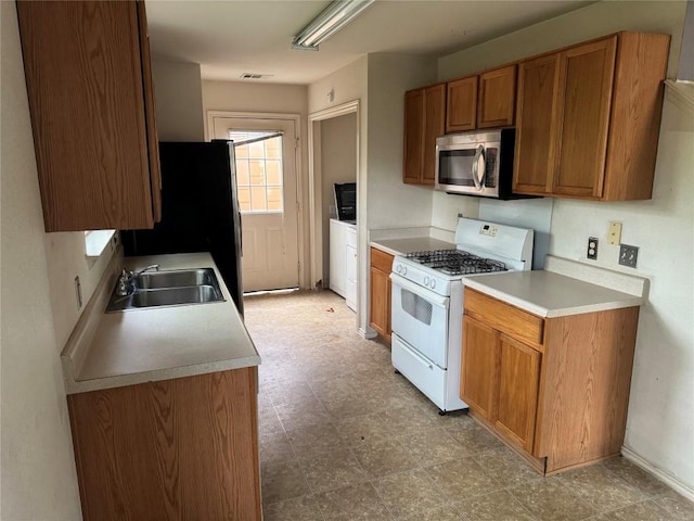 kitchen with a sink, stainless steel microwave, gas range gas stove, brown cabinets, and light countertops