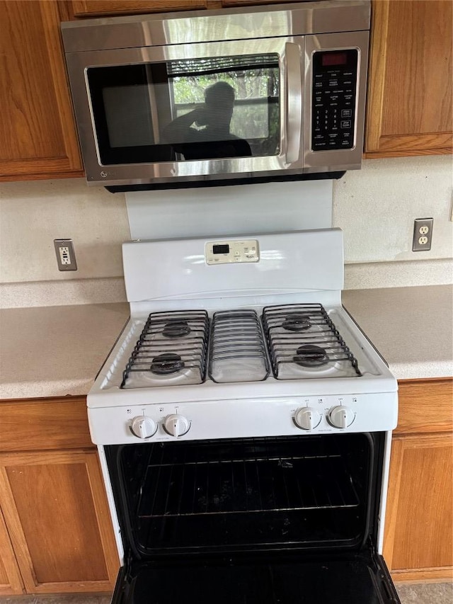 details featuring stainless steel microwave, light countertops, gas range gas stove, and brown cabinets