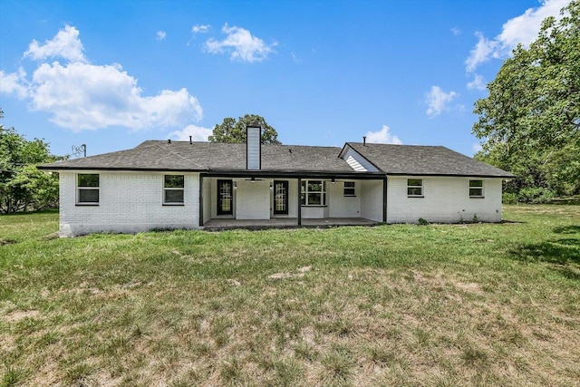 back of property with a chimney, a patio, a yard, and brick siding