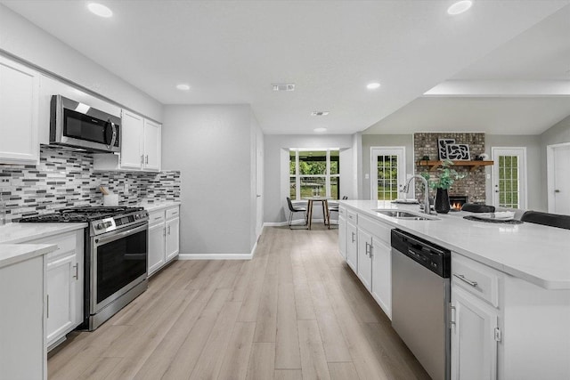 kitchen featuring light wood-style floors, tasteful backsplash, white cabinets, appliances with stainless steel finishes, and a sink