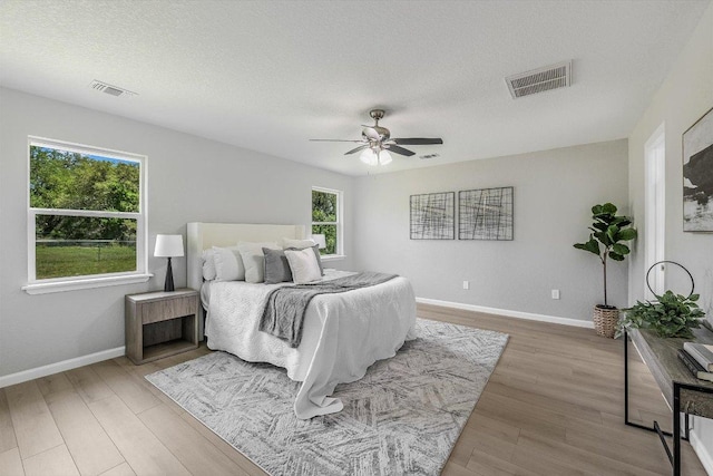 bedroom with visible vents, baseboards, light wood-style floors, and a textured ceiling
