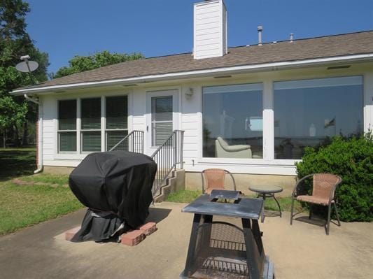 rear view of property with roof with shingles, a chimney, and a patio area