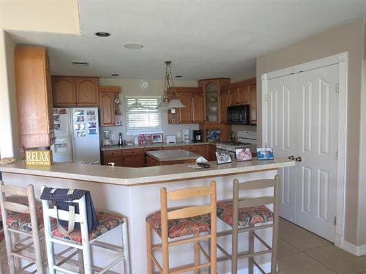 kitchen featuring gas stove, black microwave, glass insert cabinets, white refrigerator with ice dispenser, and a kitchen bar