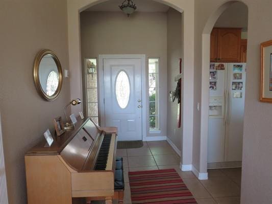 entryway with arched walkways, light tile patterned floors, and baseboards