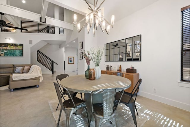 dining space featuring concrete floors, baseboards, a towering ceiling, ceiling fan with notable chandelier, and stairs