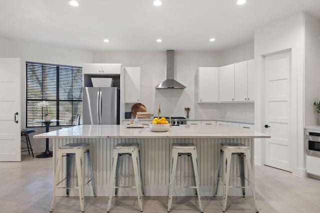 kitchen featuring wall chimney range hood, recessed lighting, white cabinetry, and freestanding refrigerator