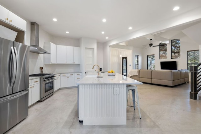 1018 Harwood Pl, Austin, TX 78704 - kitchen with wall chimney range hood, stainless steel appliances, a ceiling fan, a kitchen island with sink, and white cabinets