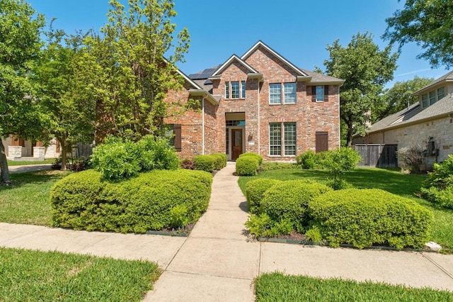 traditional-style house with solar panels, fence, a front lawn, and brick siding