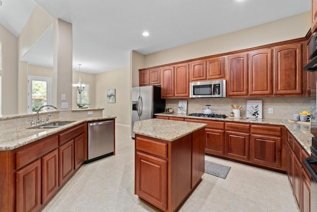 kitchen featuring a sink, appliances with stainless steel finishes, decorative backsplash, a kitchen island, and light stone counters