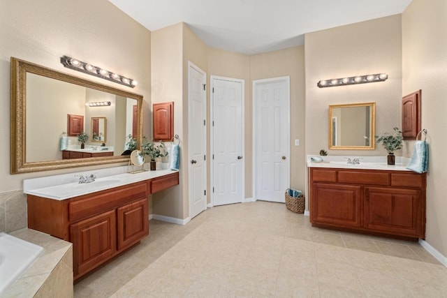 full bath with a sink, two vanities, a relaxing tiled tub, and baseboards